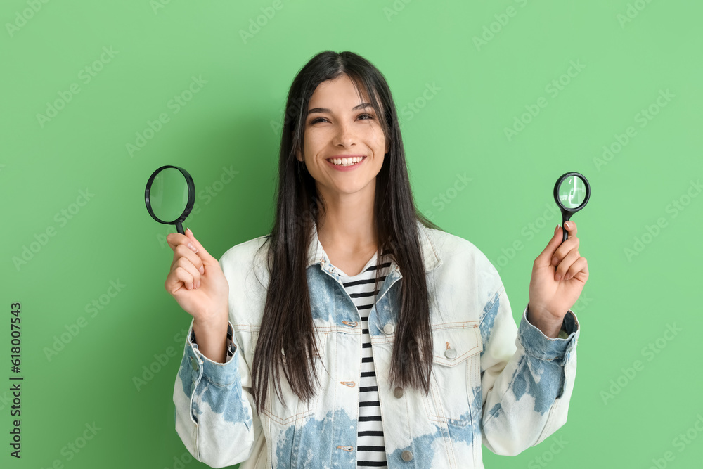 Beautiful happy young woman with magnifier on green background