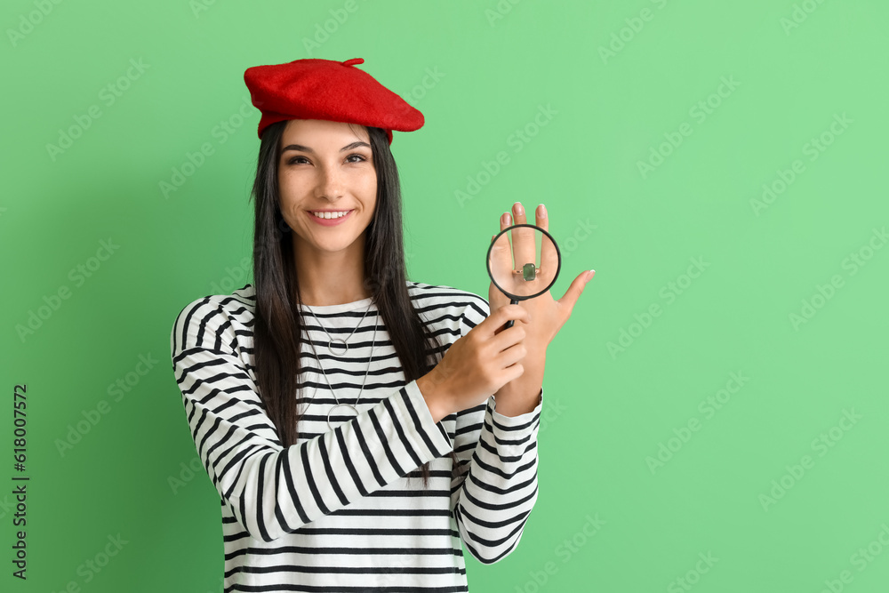 Beautiful young woman with magnifier and gold ring of gem on green background