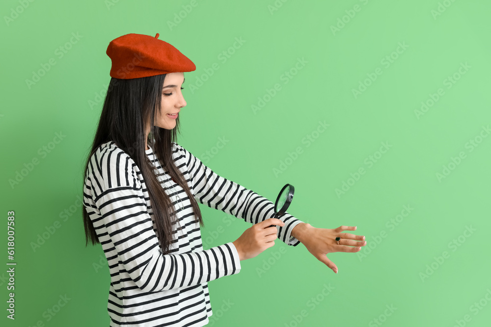 Beautiful happy young woman with magnifier and gold ring of gem on green background