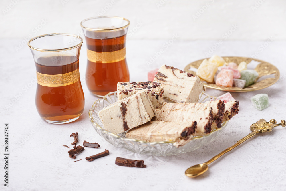 Pieces of tasty marble halva and glasses with Turkish tea on light background