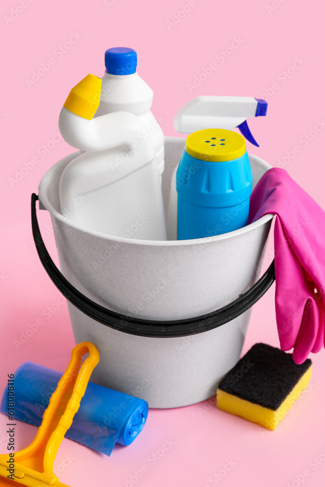 Bucket with different cleaning supplies on pink background