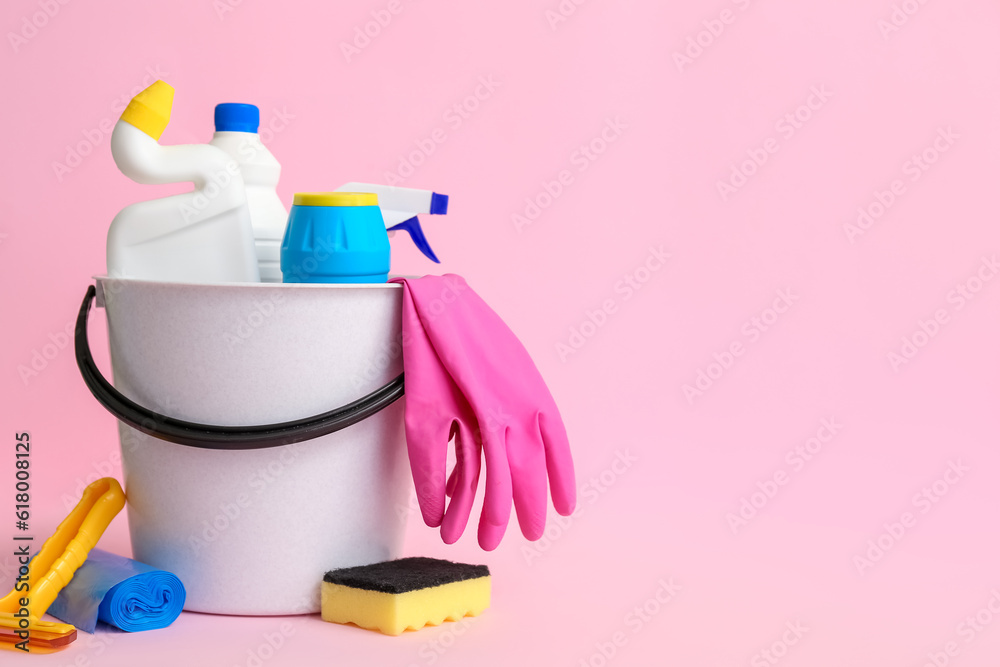 Bucket with different cleaning supplies on pink background