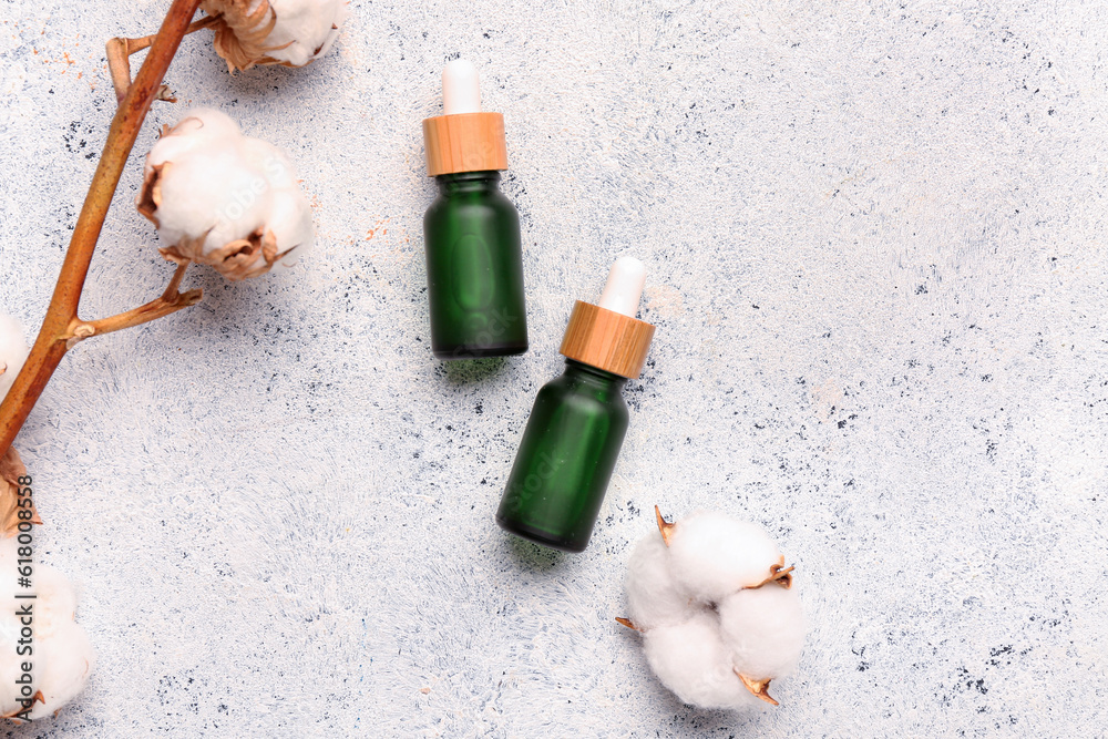 Bottles of essential oil and cotton branch on light background