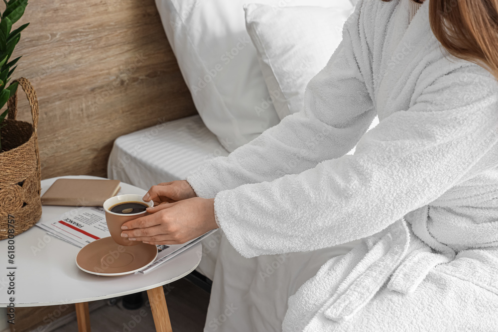 Woman in bathrobe taking cup of delicious coffee from table