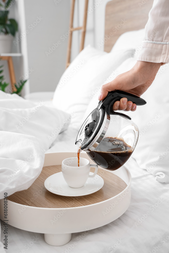 Woman pouring coffee from pot into cup in bed