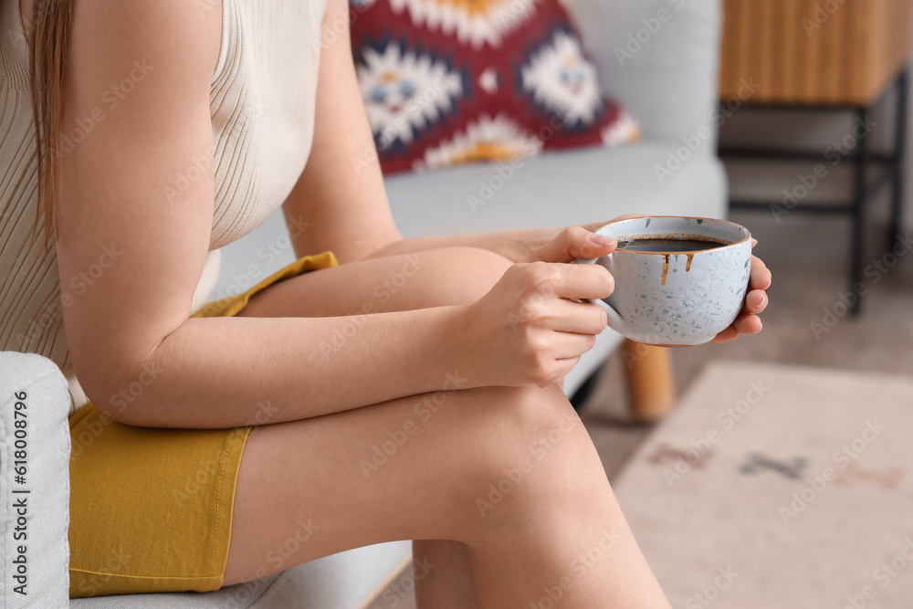 Woman sitting on cozy sofa and holding cup of delicious coffee