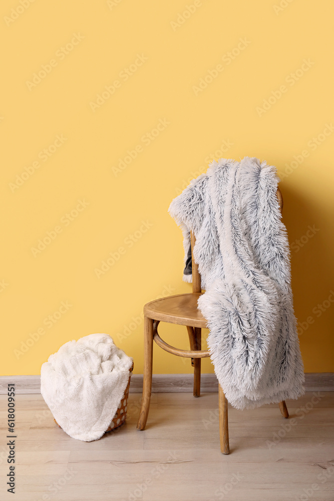 New soft blankets on chair and basket near yellow wall in room