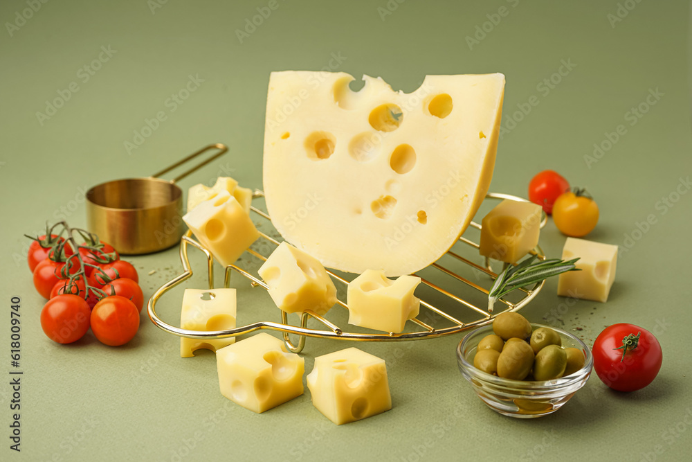 Stand with pieces of Swiss cheese and olives on green background