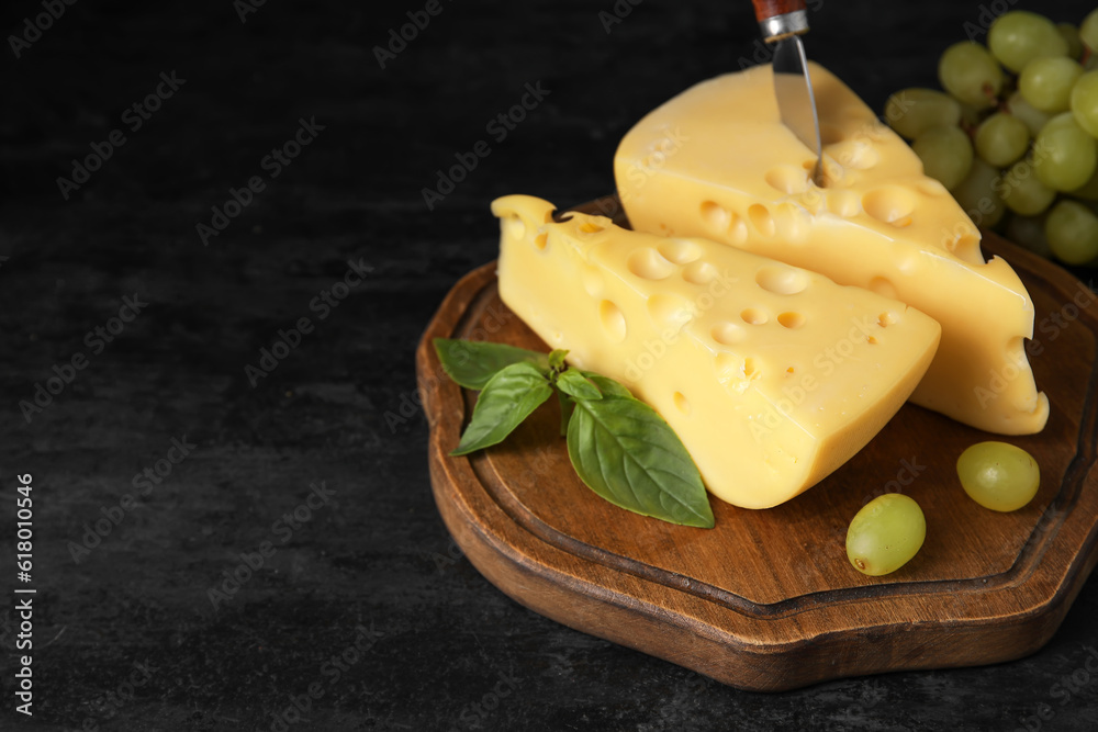 Board with tasty Swiss cheese on black background