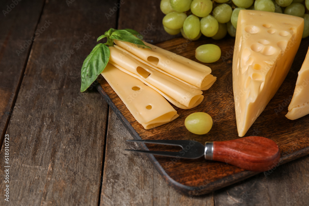 Board with tasty Swiss cheese and grapes on wooden background