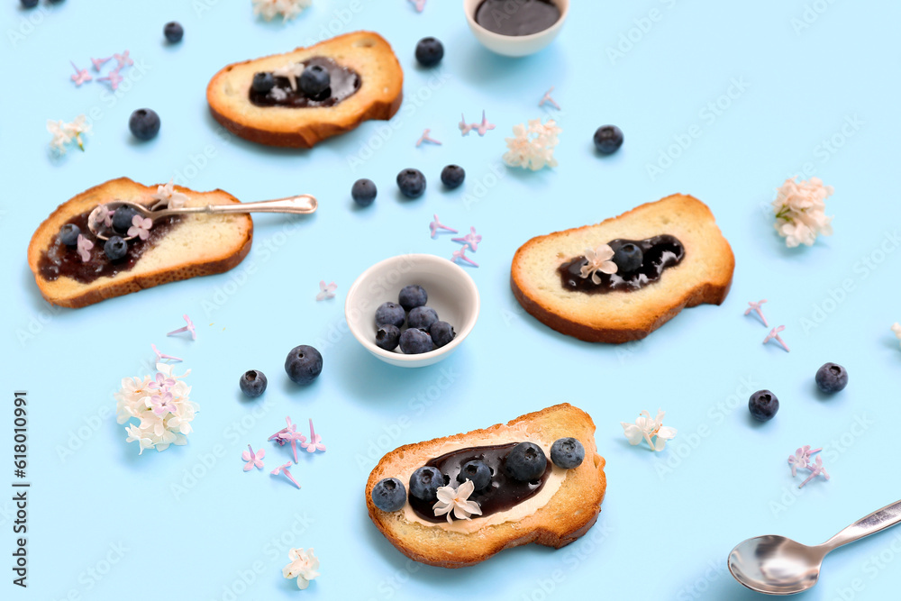 Composition with delicious jam toasts, blueberries and flowers on blue background