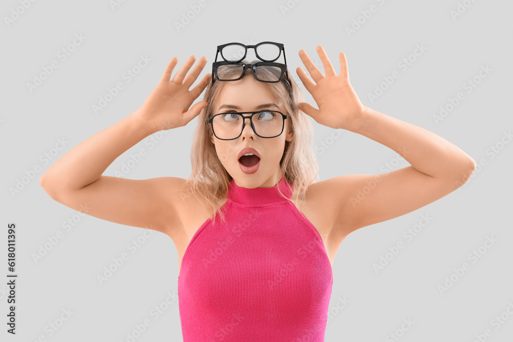 Shocked young woman in stylish eyeglasses on light background