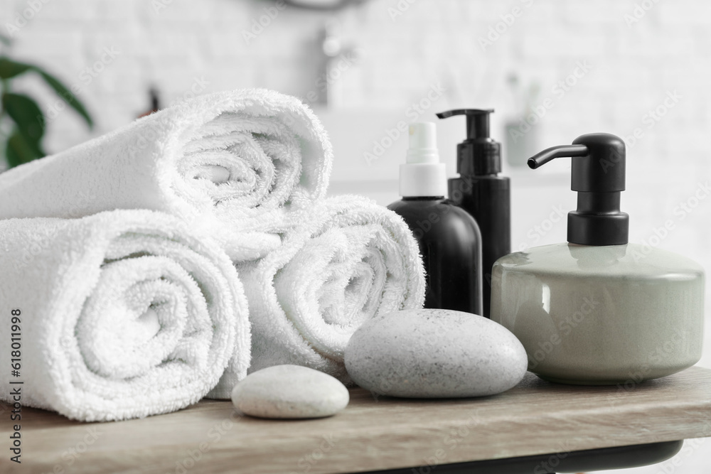 Soap dispenser, pebbles and rolled towels on table in bathroom, closeup