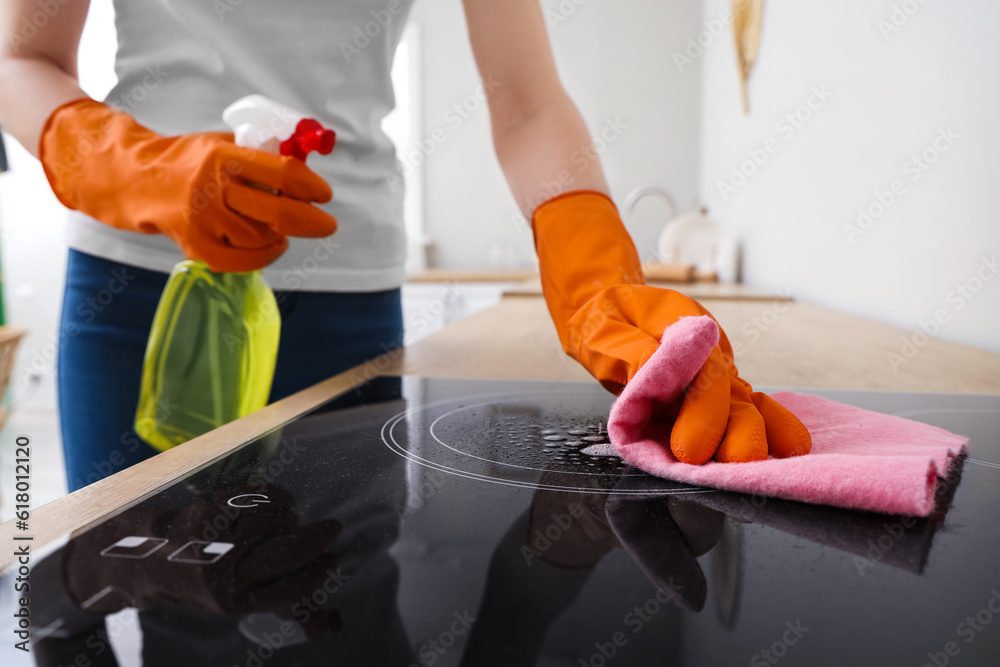 Woman in orange rubber gloves cleaning electric stove with rag and detergent