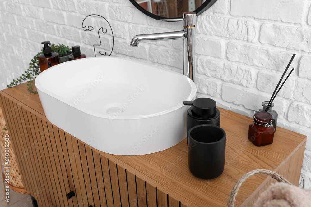 Sink bowl with bath accessories on wooden cabinet in bathroom, closeup