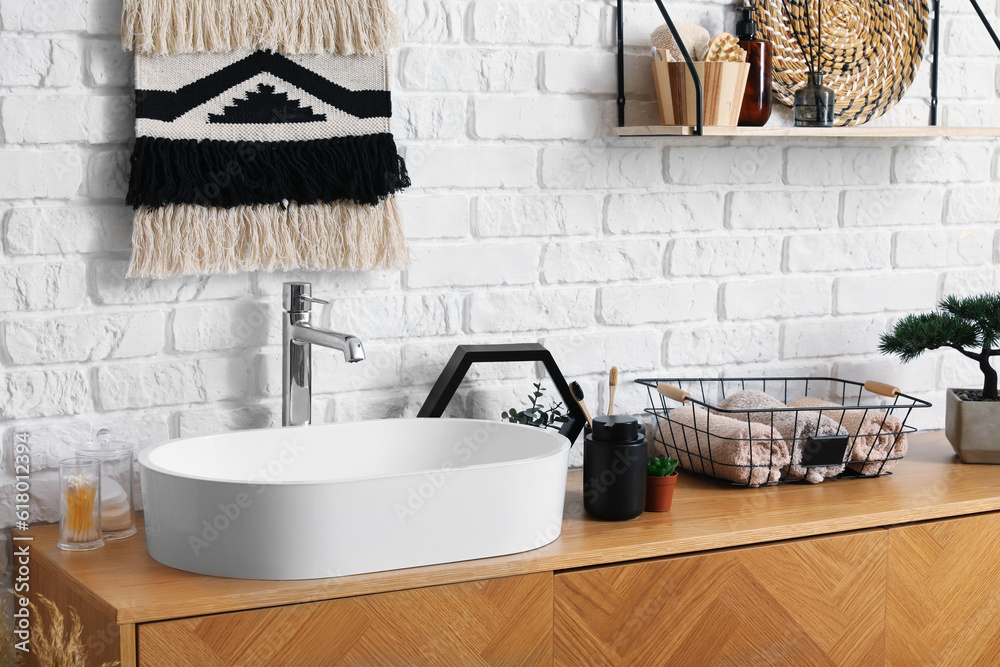 Sink bowl and bath accessories on wooden cabinet in bathroom