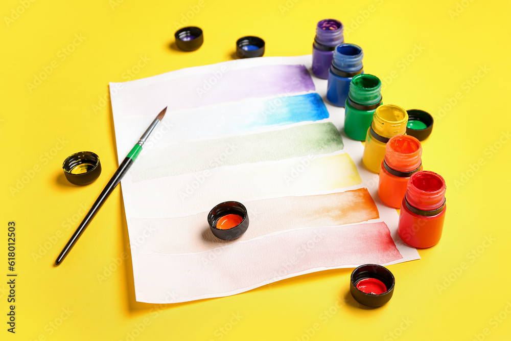 Composition with different paints, brush and rainbow color palette on yellow background