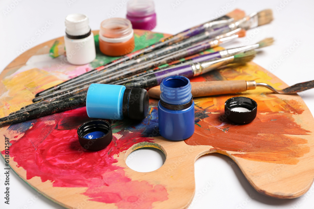 Wooden palette with different paints and brushes isolated on white background