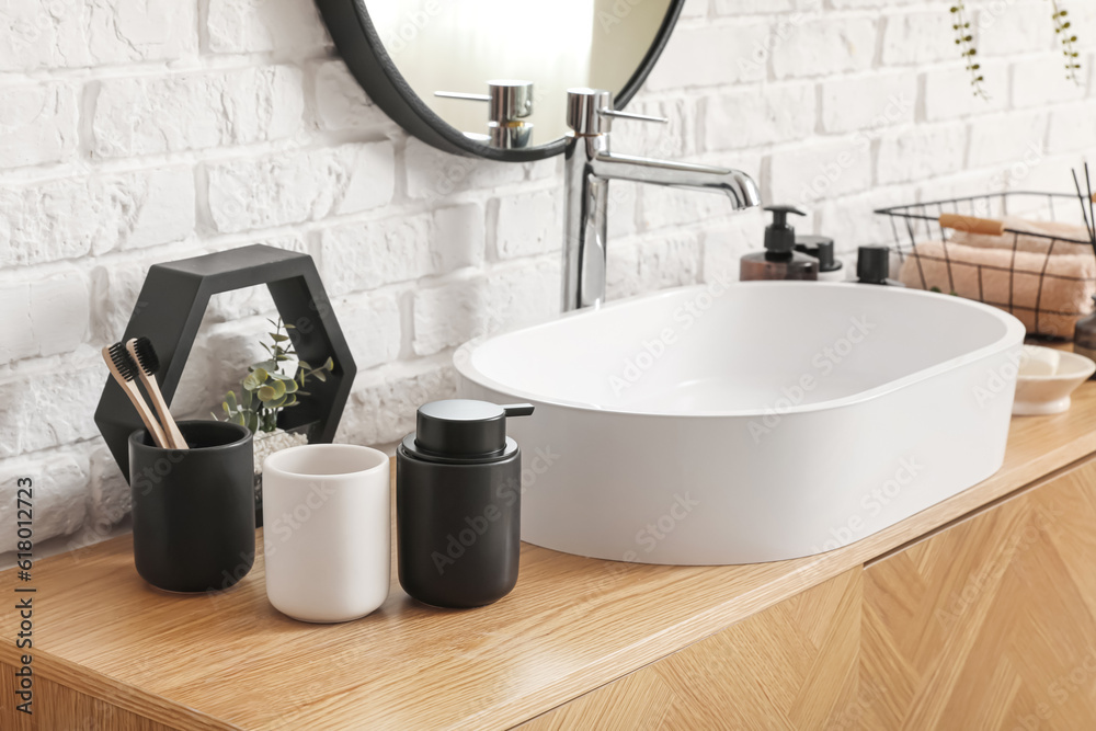 Sink bowl and bath accessories on wooden cabinet near white brick wall