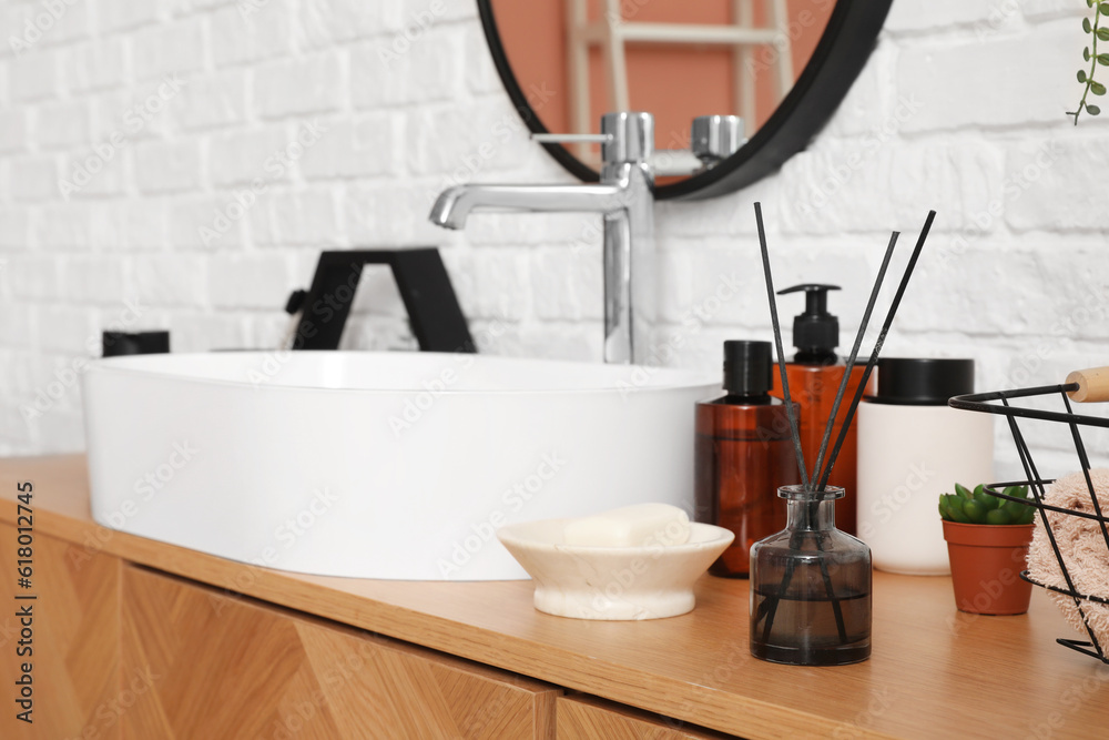 Sink bowl and bath accessories on wooden cabinet near white brick wall