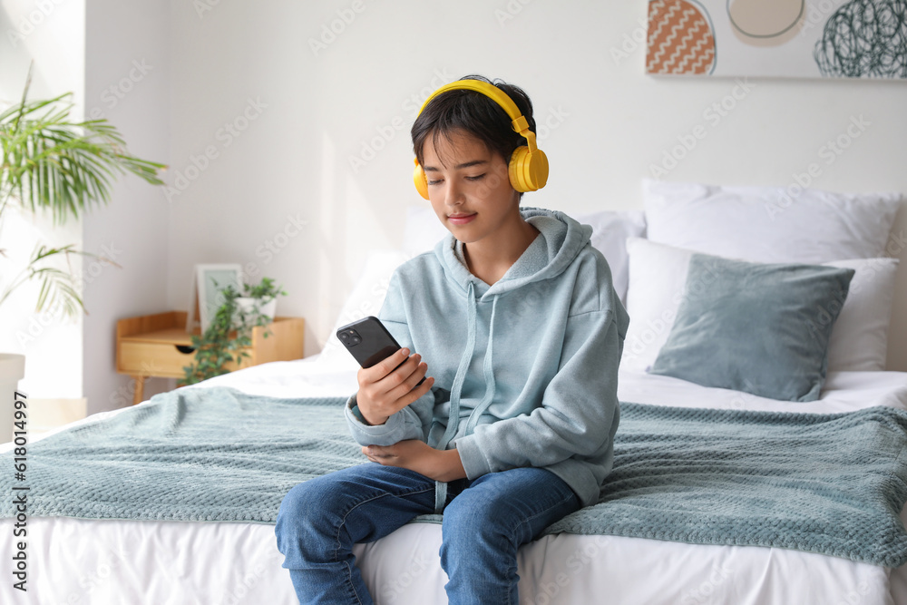 Little boy with headphones using mobile phone in bedroom