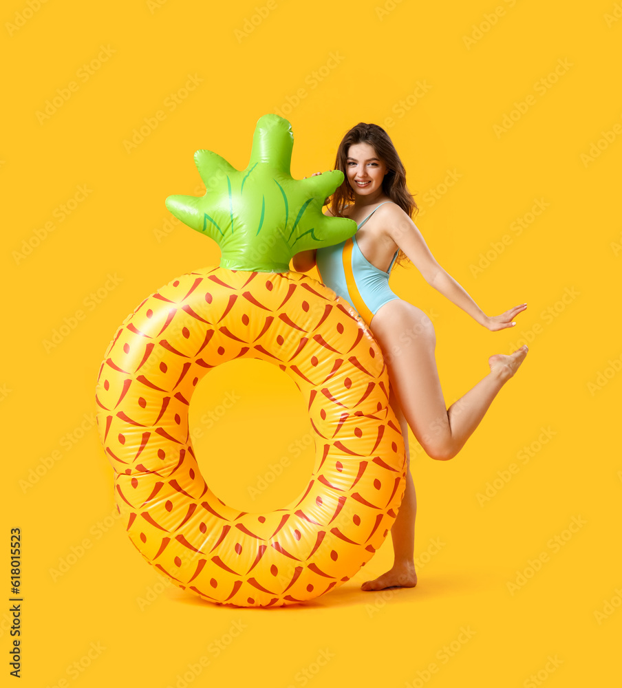 Young woman with swim ring in shape of pineapple on yellow background