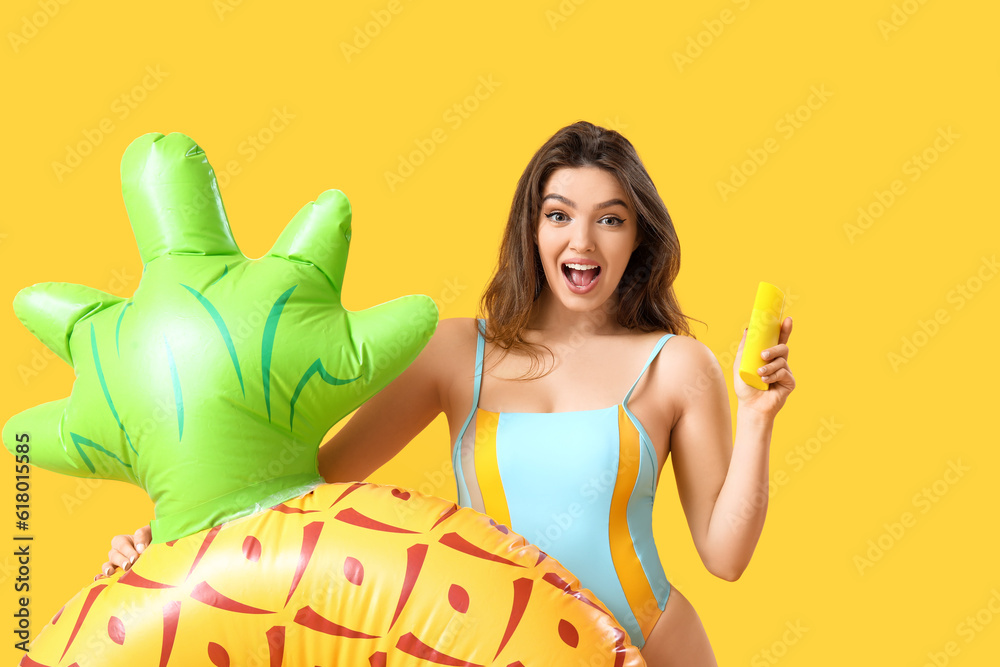 Young woman with swim ring in shape of pineapple and sunscreen cream on yellow background