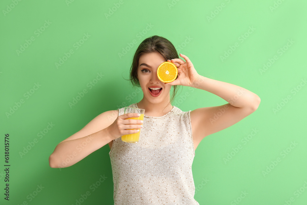 Young woman with glass of juice and orange on green background