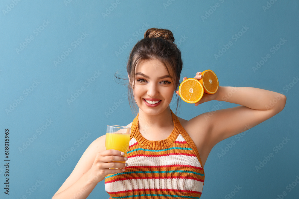 Young woman with glass of juice and oranges on blue background