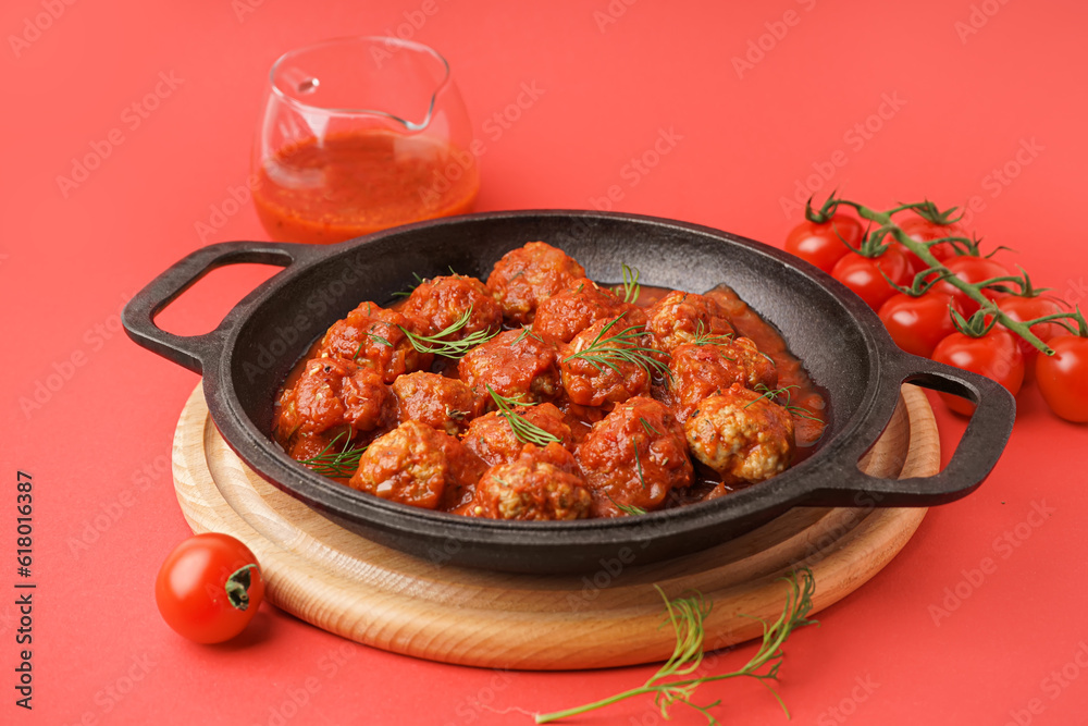 Frying pan of tasty meat balls with tomato sauce and dill on red background