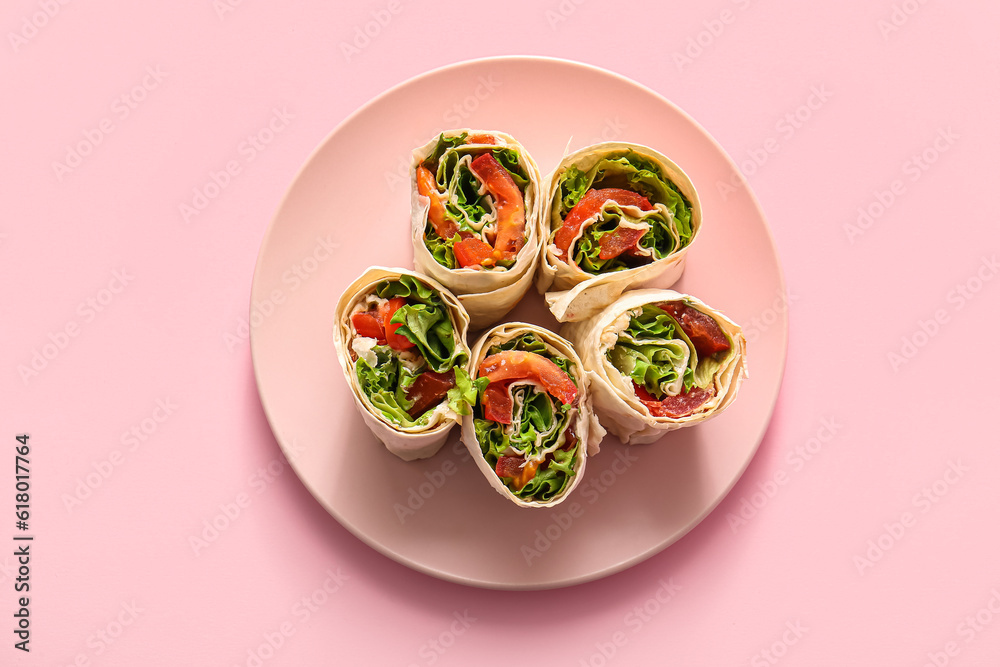 Plate of tasty lavash rolls with tomatoes and greens on pink background