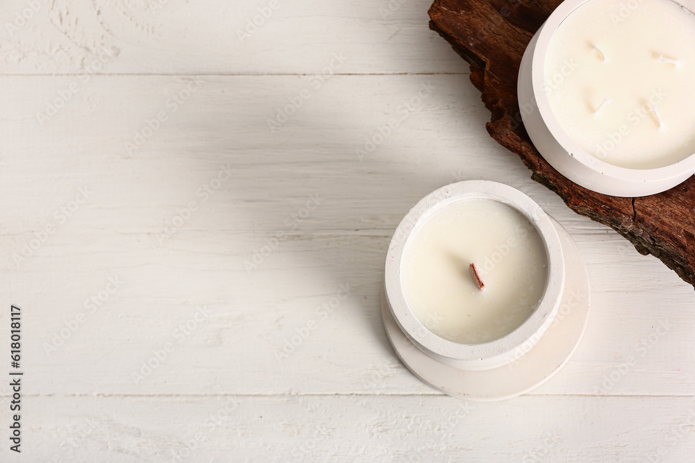 Holders with candles and tree bark on white wooden background