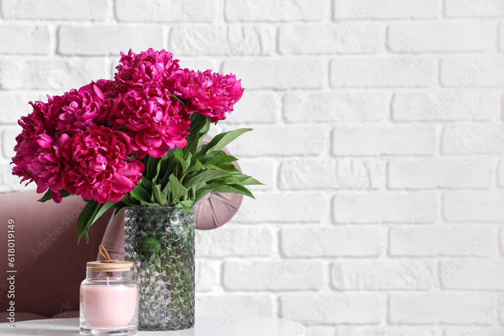 Vase of red peonies with candle on coffee table and couch near white brick wall