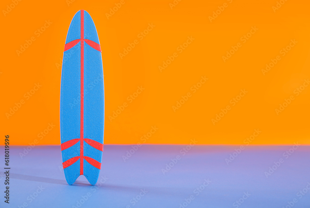 Mini surfboard on blue table against orange background