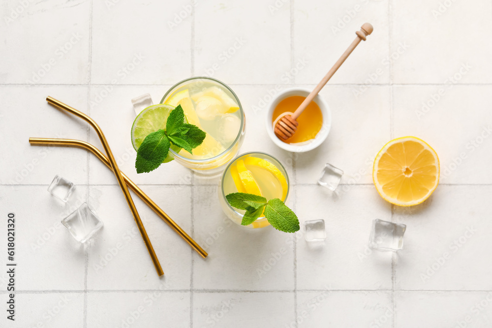 Glasses of infused water with lemon and honey on white tile background