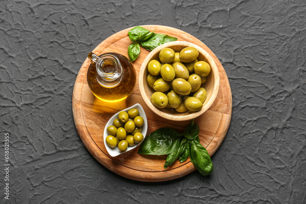 Bowls with ripe olives and jug of oil on black background