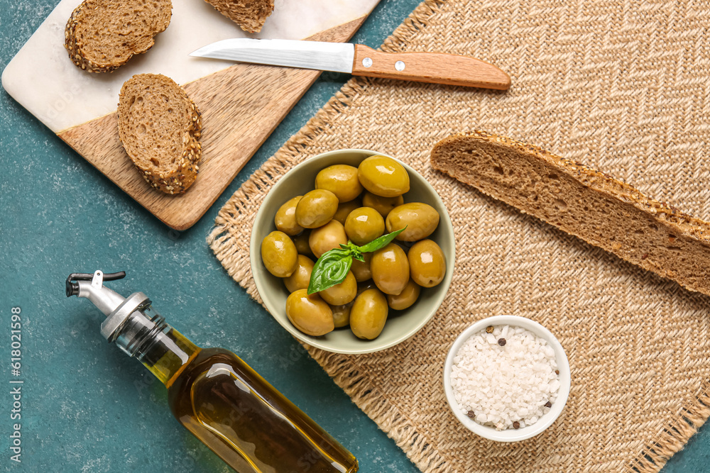 Bowl with ripe olives, bread and bottle of oil on green background