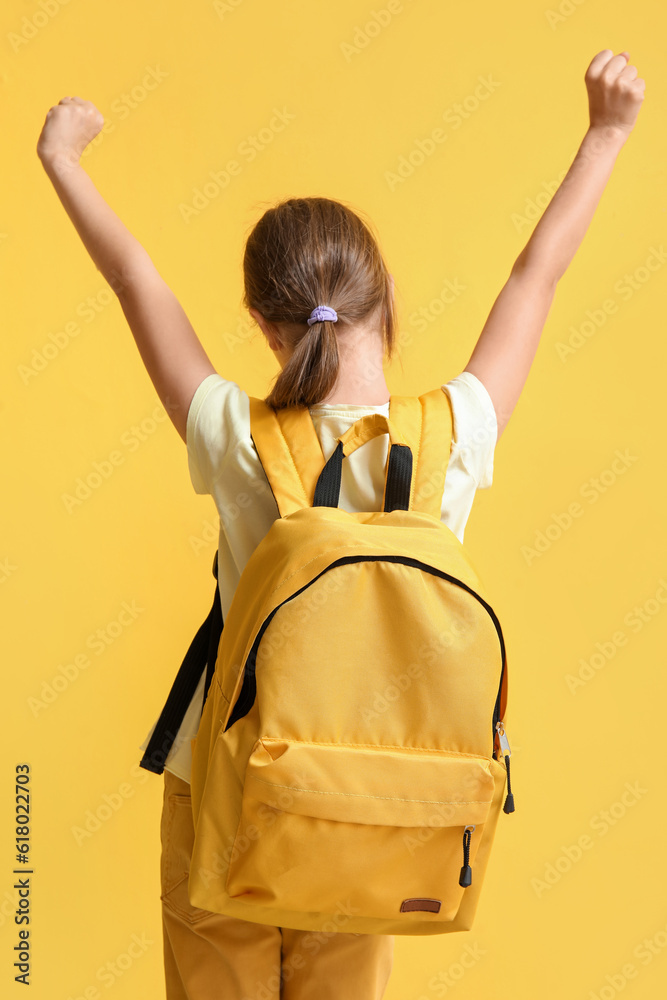 Little girl with backpack on yellow background, back view