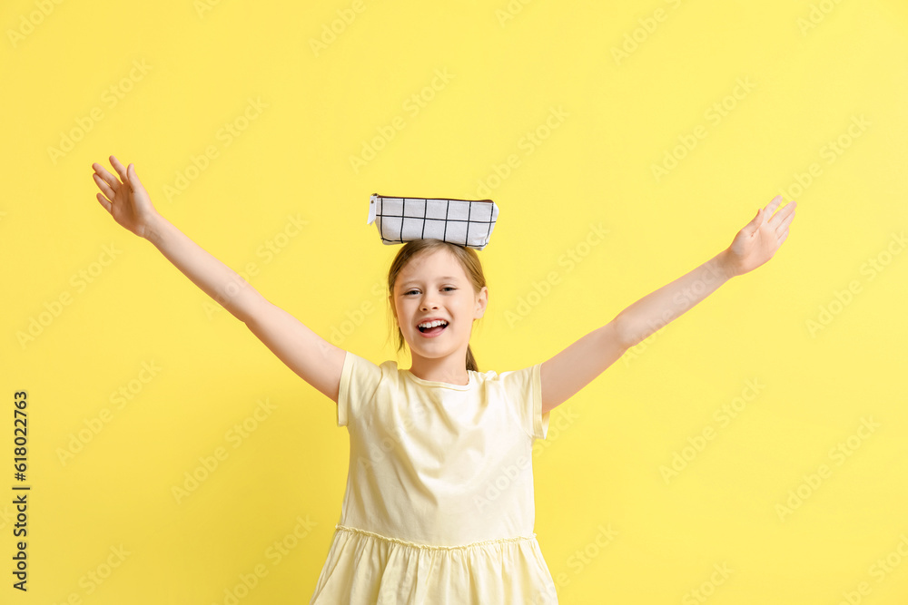 Little girl with pencil case on yellow background