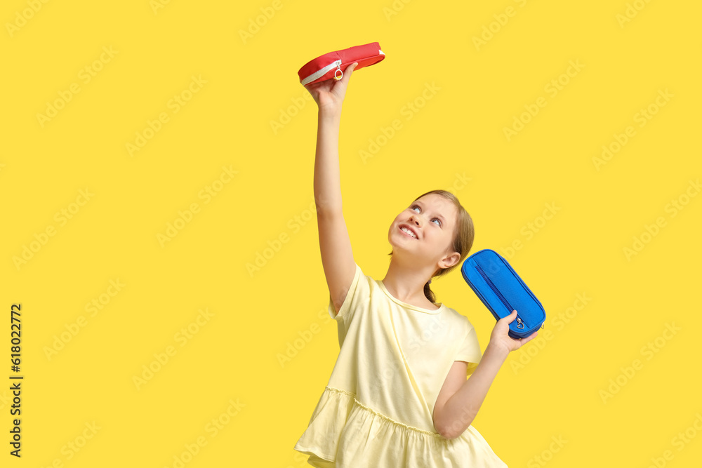 Little girl with pencil cases on yellow background