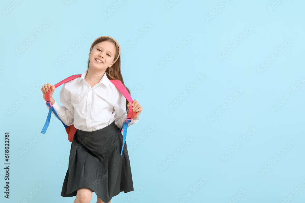 Little schoolgirl with backpack on blue background