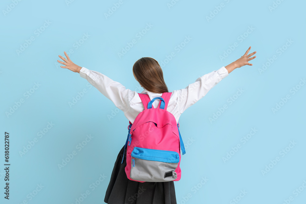 Little schoolgirl with backpack on blue background, back view