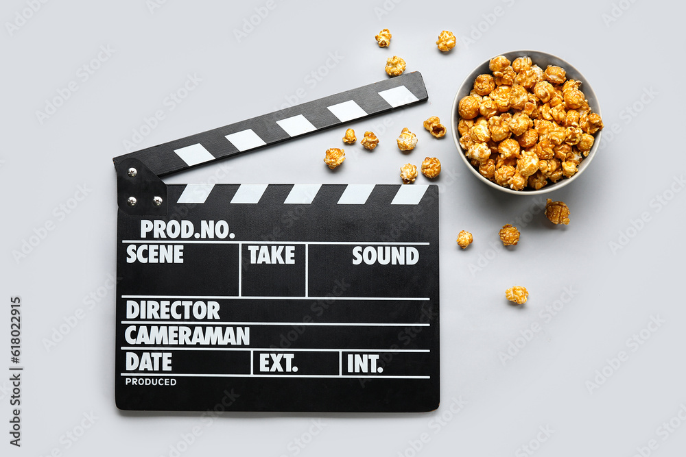 Bowl with tasty popcorn and clapperboard on grey background