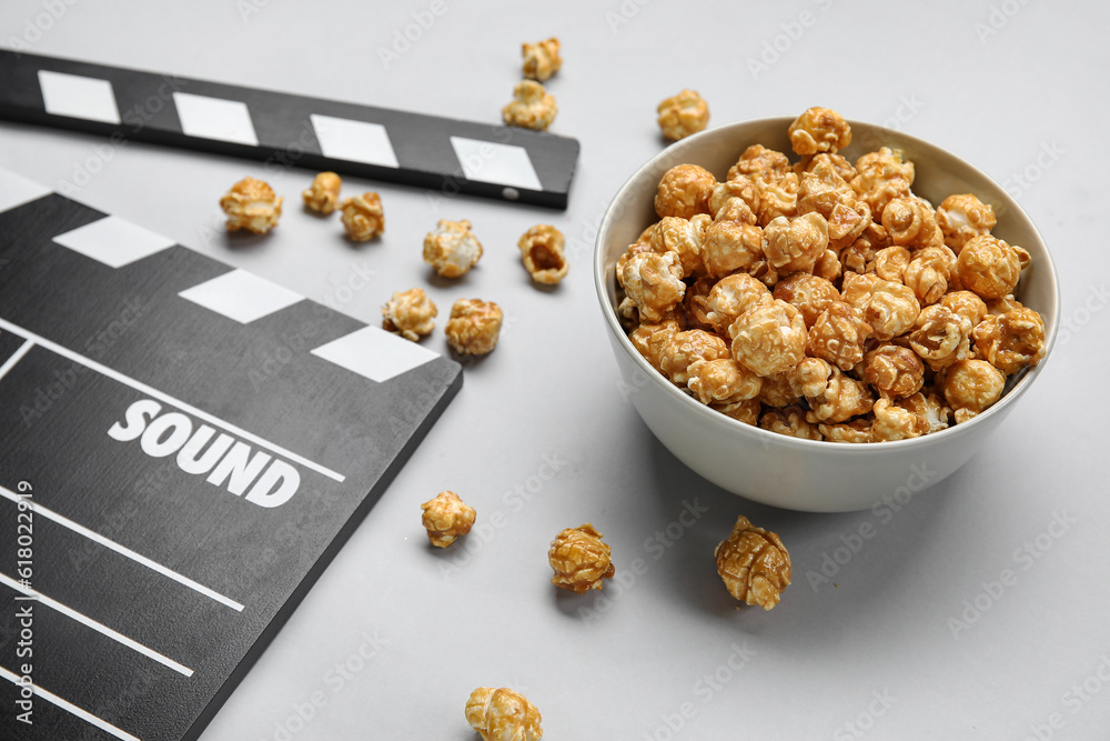 Bowl with tasty popcorn and clapperboard on grey background