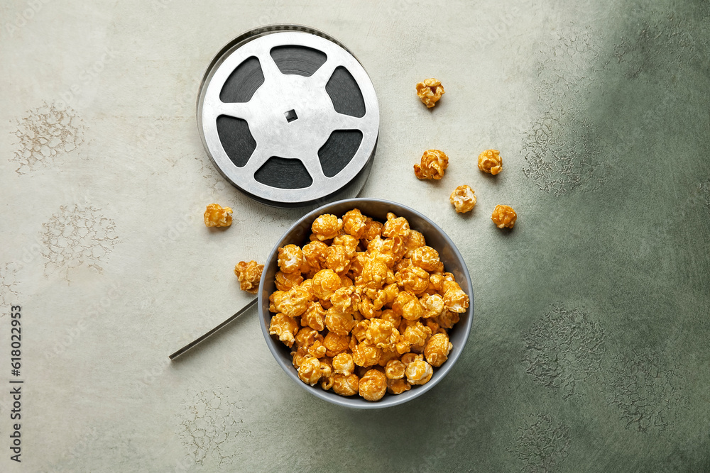 Bowl with tasty popcorn and film reel on grey background