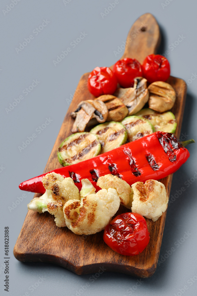 Wooden board with grilled vegetables on grey background