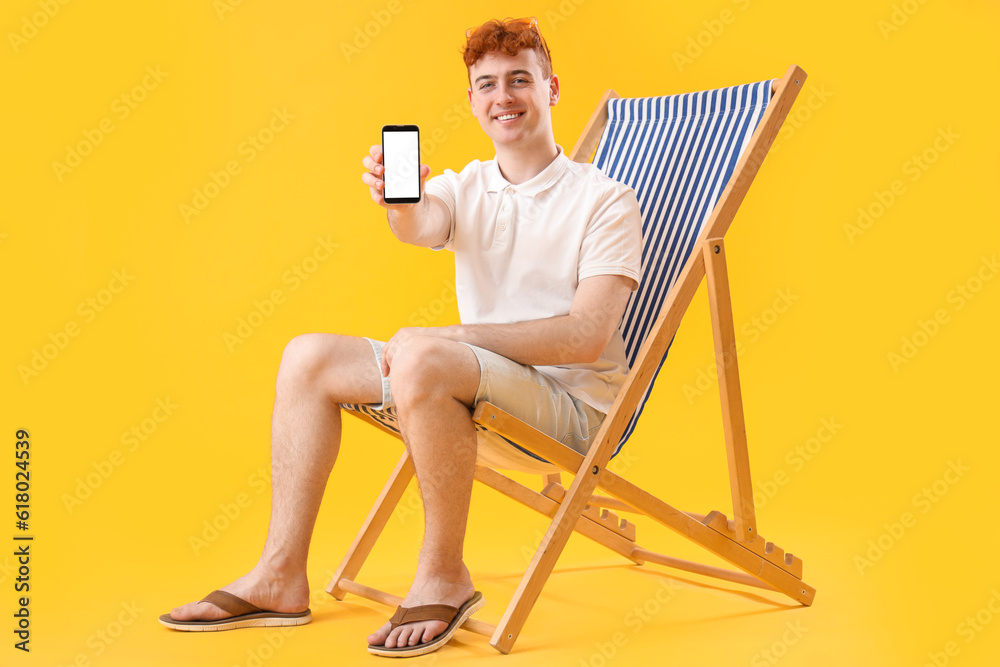 Young man with mobile phone resting in deck chair on yellow background