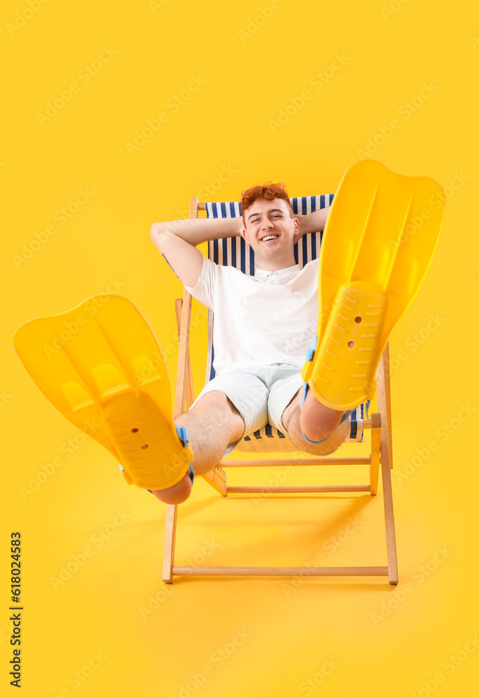 Young man with flippers resting in deck chair on yellow background