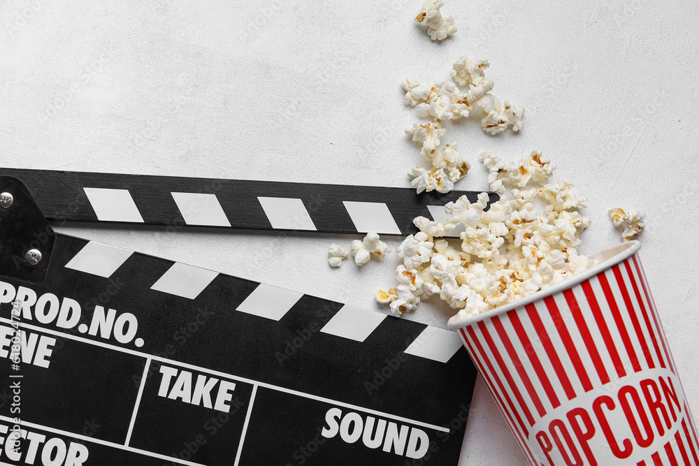 Bucket with tasty popcorn and clapperboard on white background