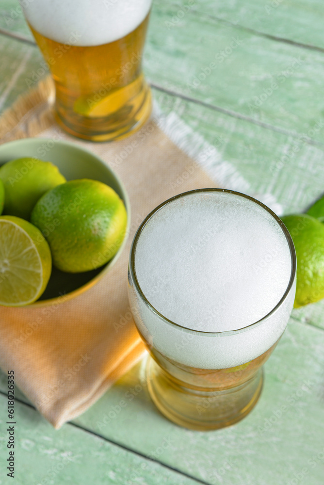 Glasses of cold beer with lime on green wooden background